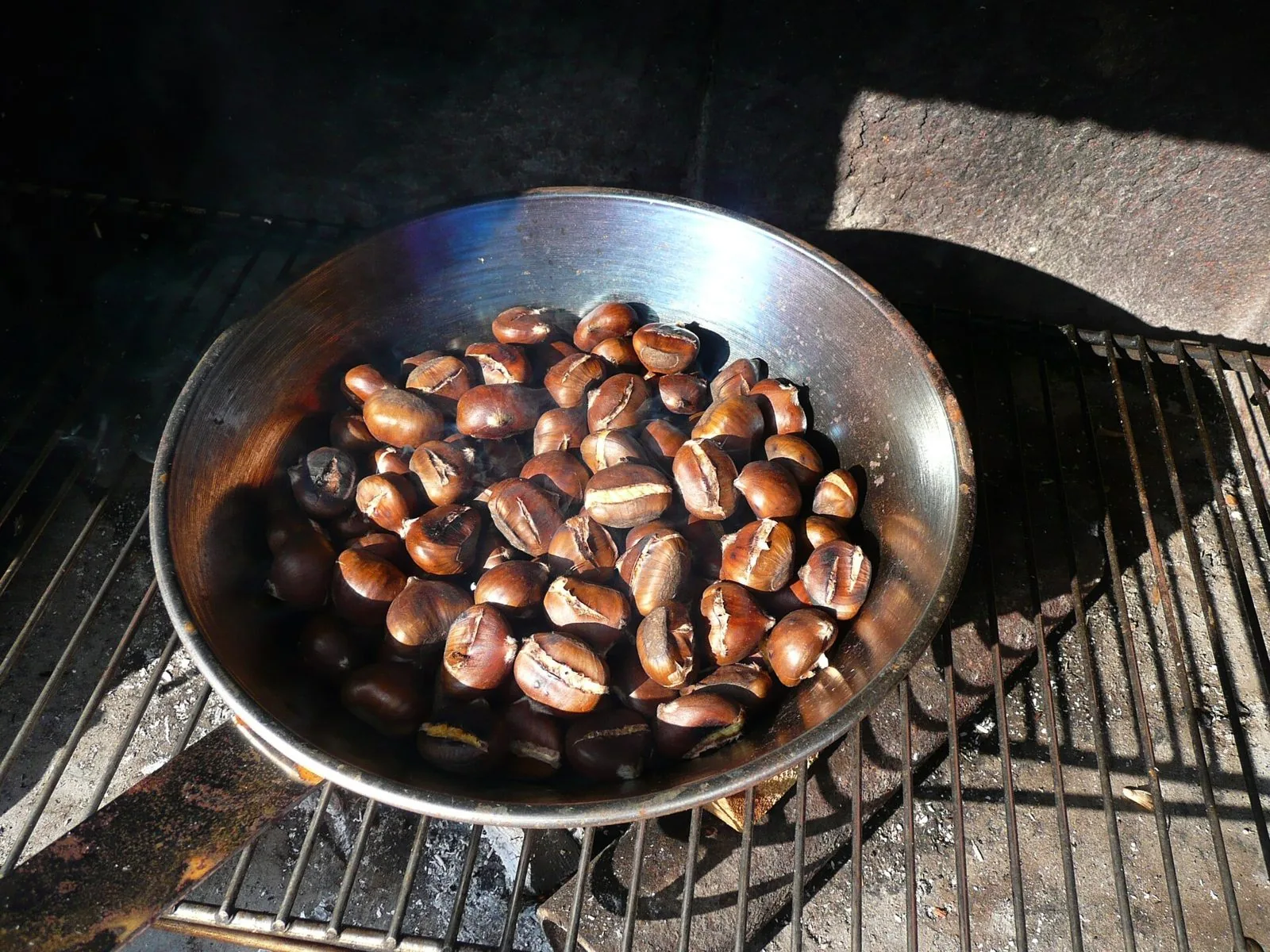 Castagne incise che arrostiscono in una padella sulla griglia, sopra la brace