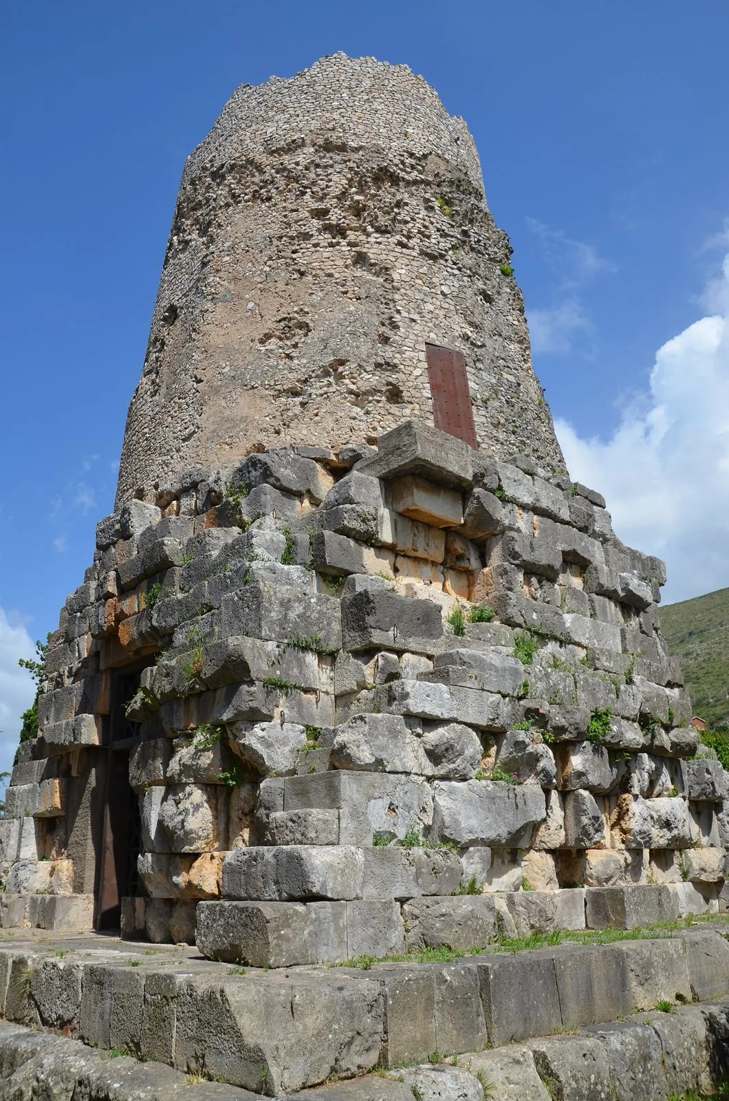 Il mausoleo noto come Tomba di Cicerone a Formia: basamento in grandi blocchi di pietra e torre cilindrica sotto un cielo azzurro